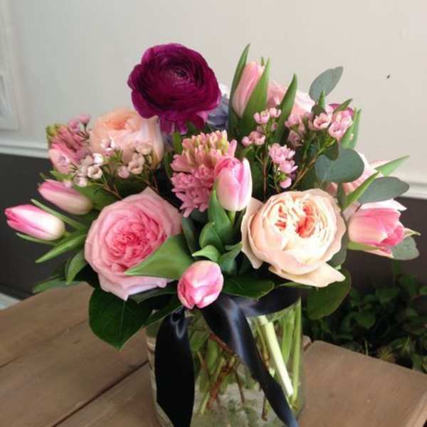 Pink roses, tulips, and mixed blooms in a clear glass vase tied with a black ribbon