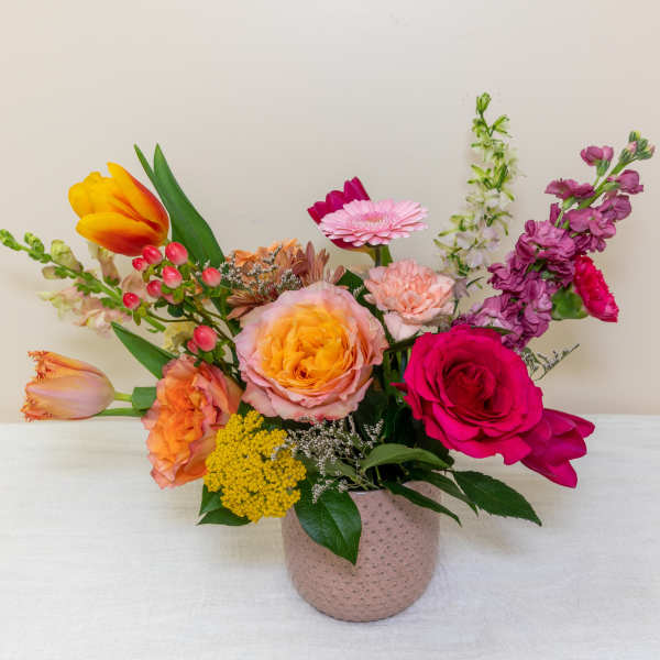 Mixed bouquet in a pink textured vase with roses, tulips, and gerbera daisies