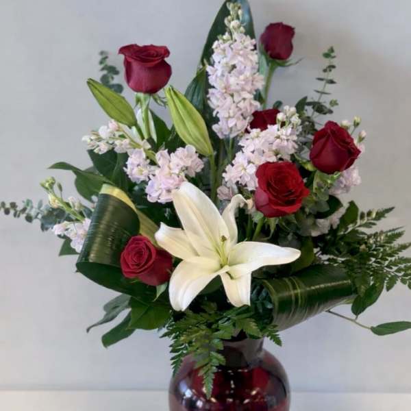 Red roses and a white lily arranged in a burgundy glass vase