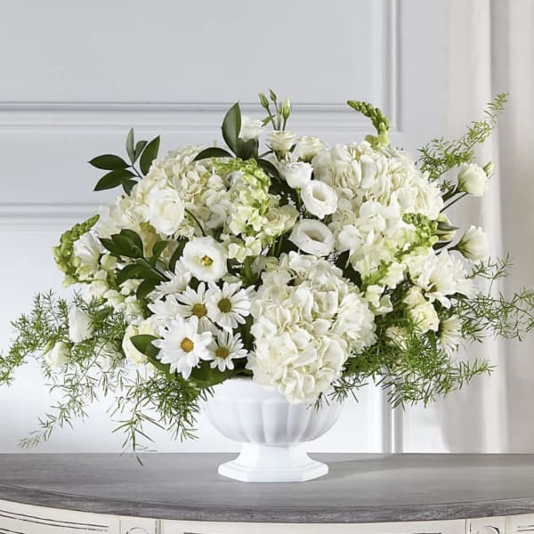 White floral arrangement in a white pedestal vase with daisies and hydrangeas