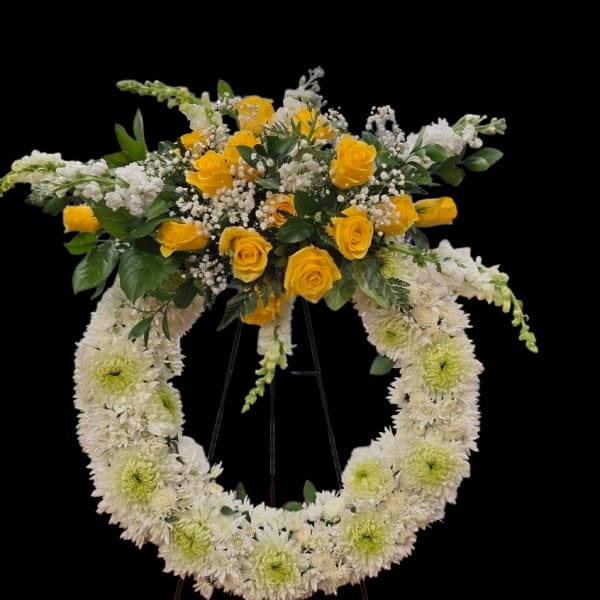 Standing white chrysanthemum wreath with yellow roses and white flowers on a metal easel.