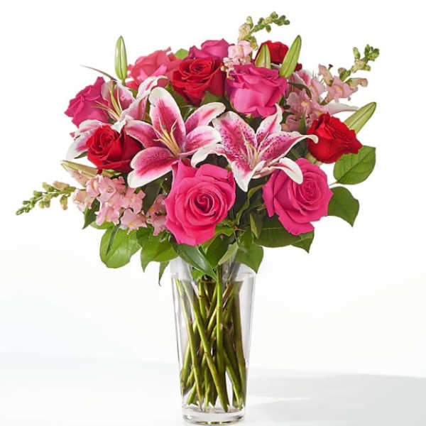 Tall glass vase of red and hot pink roses with pink lilies and snapdragons.