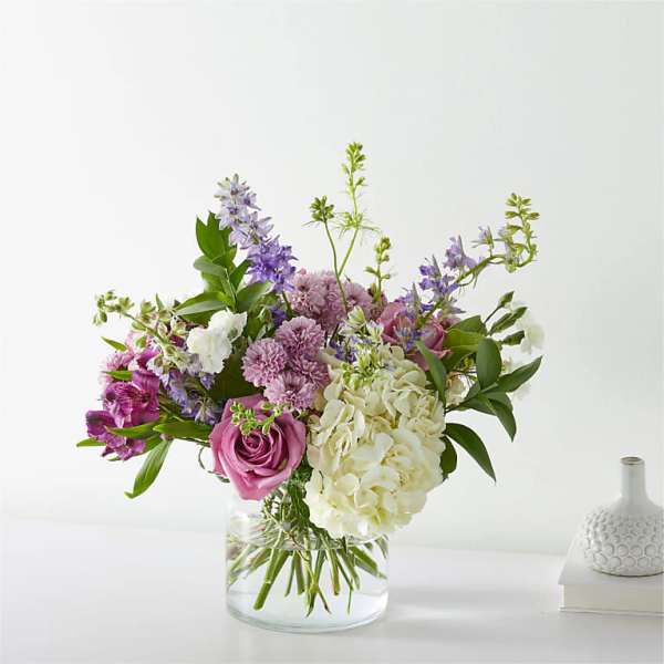 Mixed bouquet of purple, pink, and white flowers in a clear glass vase