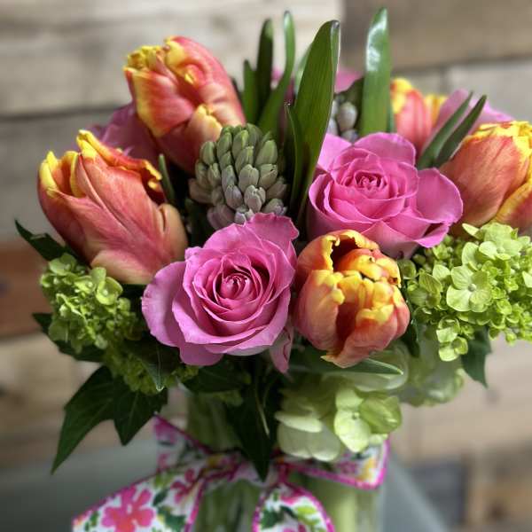 Bright bouquet of pink roses, orange-yellow tulips, and green hydrangeas in a glass vase with a floral bow
