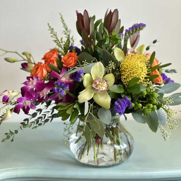 Mixed bouquet in a clear glass vase with orchids, roses, and yellow pincushion blooms