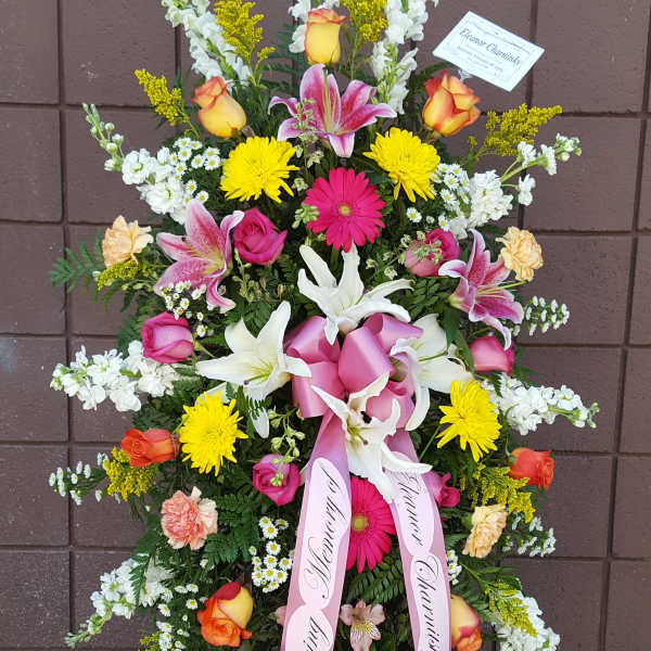 Tall standing spray of mixed flowers with pink ribbons on an easel