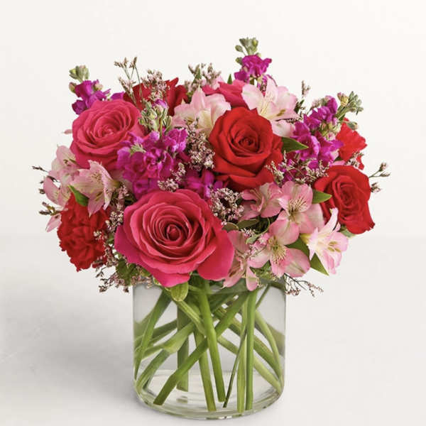 Pink and red roses with pale pink lilies in a clear glass vase