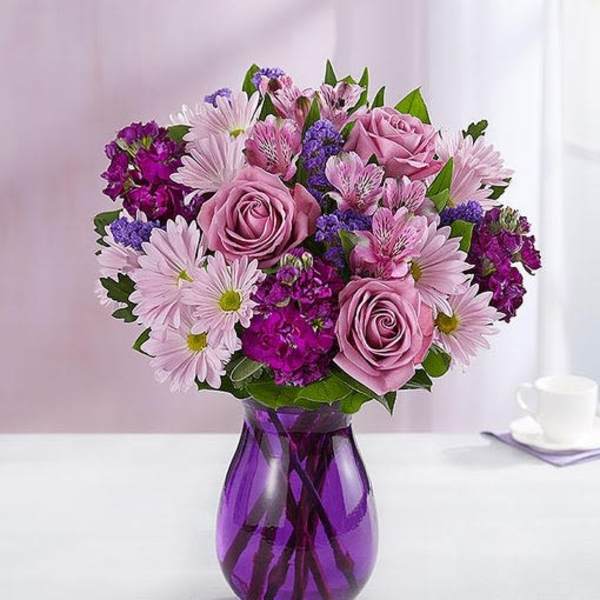 Lavender and purple mixed bouquet with roses and daisies in a purple glass vase