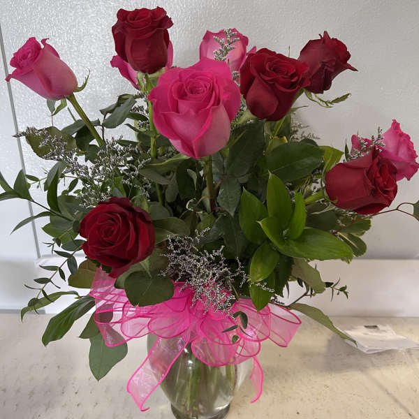 Bouquet of pink and red roses in a clear glass vase with a pink ribbon