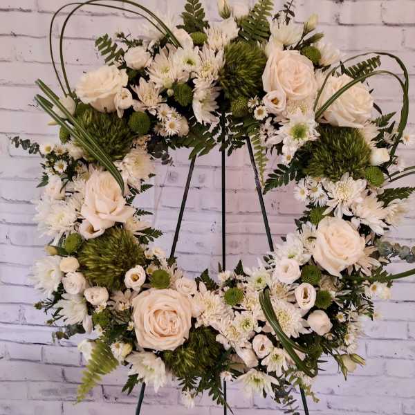 White floral wreath on a metal stand with roses and daisies
