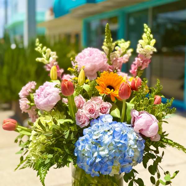Mixed bouquet in a glass vase with blue hydrangea, pink roses, tulips, and orange gerbera daisies