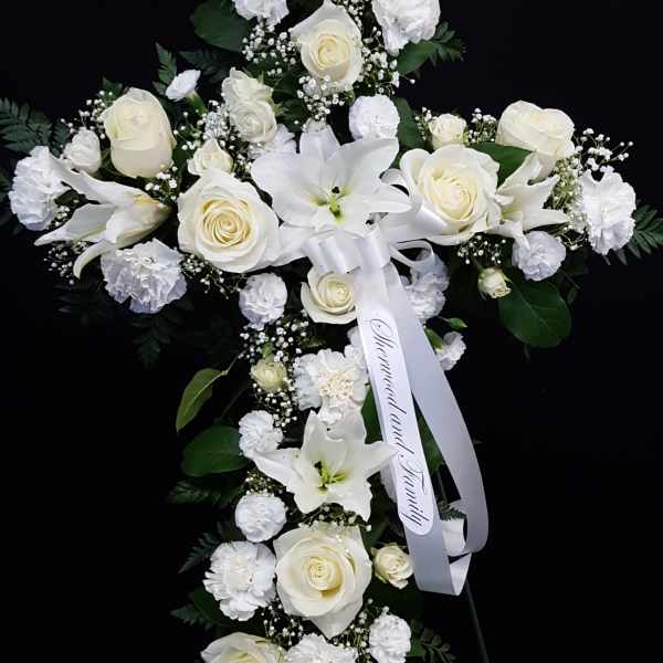 White floral standing spray with roses, lilies, and carnations on a black background