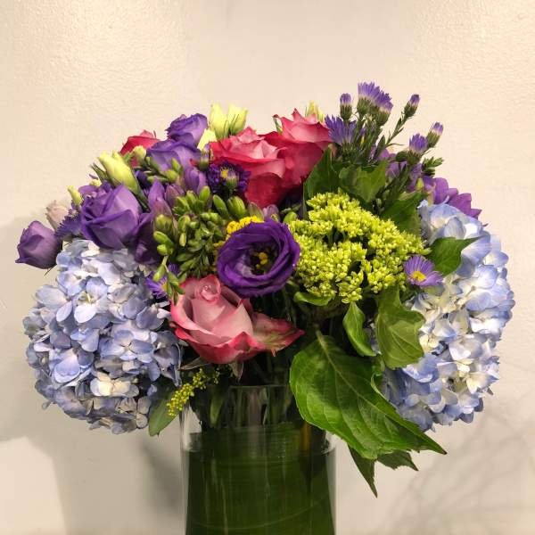 Mixed bouquet of roses, hydrangeas, and purple flowers in a glass vase