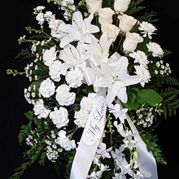 White funeral spray with lilies, roses, and carnations on a black background