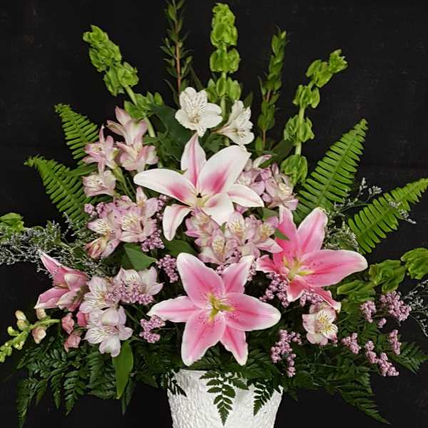 Pink lilies and small white flowers arranged in a white vase