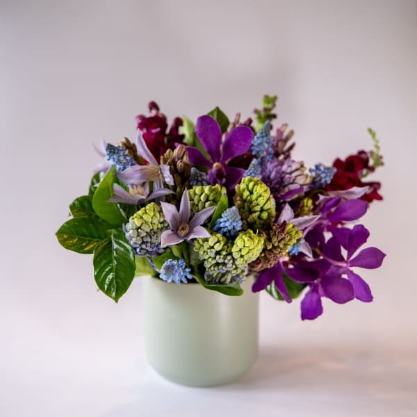 Purple and blue mixed bouquet in a pale green vase