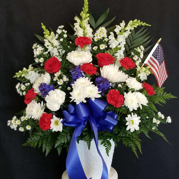Red, white, and blue floral arrangement in a white vase with an American flag