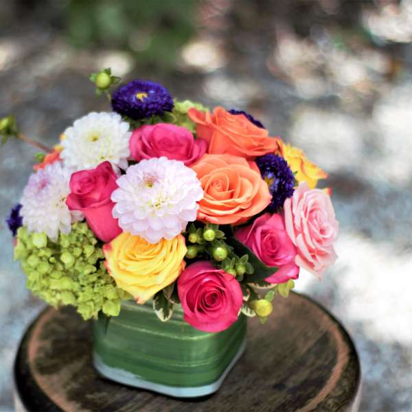Colorful bouquet of roses and pom-pom flowers in a green vase
