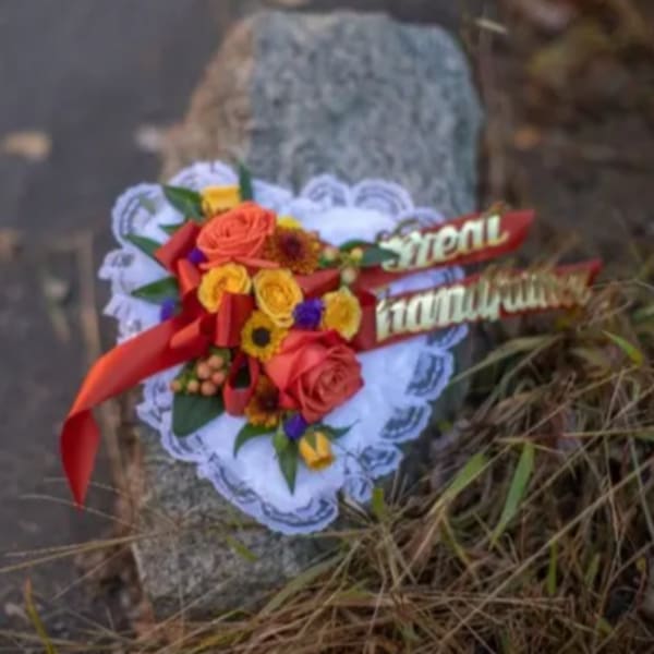 Heart-shaped floral tribute with red and yellow roses and a red ribbon