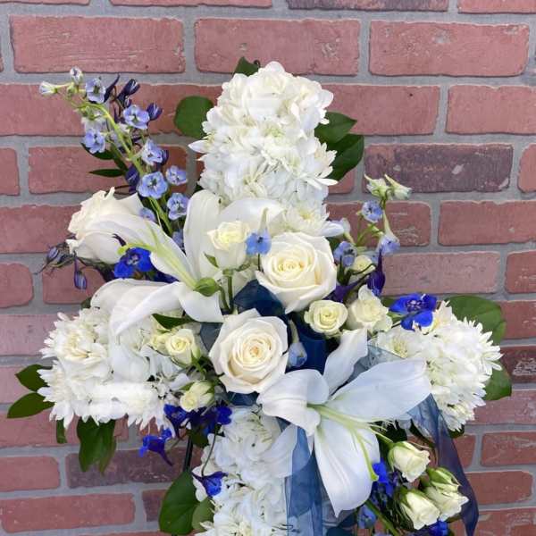 White floral standing spray with blue accents on an easel