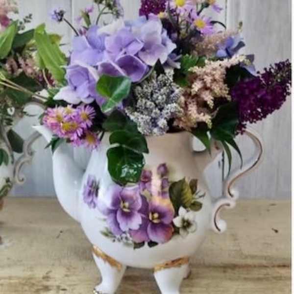 Purple floral arrangement in a white ceramic pitcher vase
