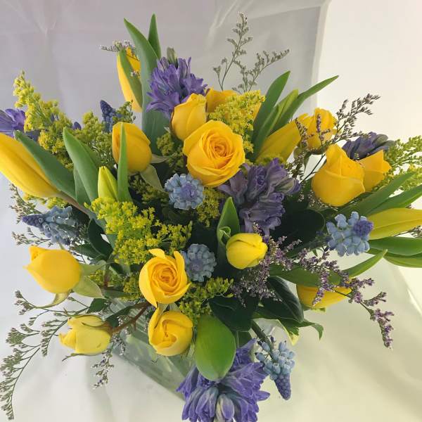 Arrangement of yellow roses and tulips with purple hyacinths in a clear glass vase
