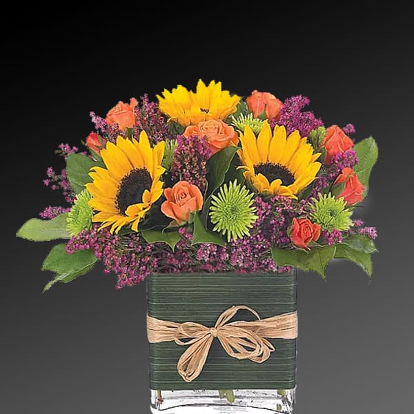 Sunflowers and orange roses in a square glass vase with a ribbon