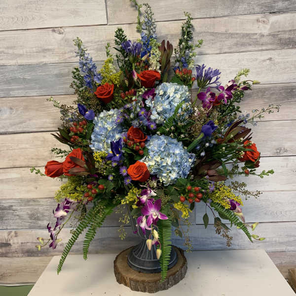 Large mixed floral arrangement in a pedestal vase with blue hydrangeas and red roses