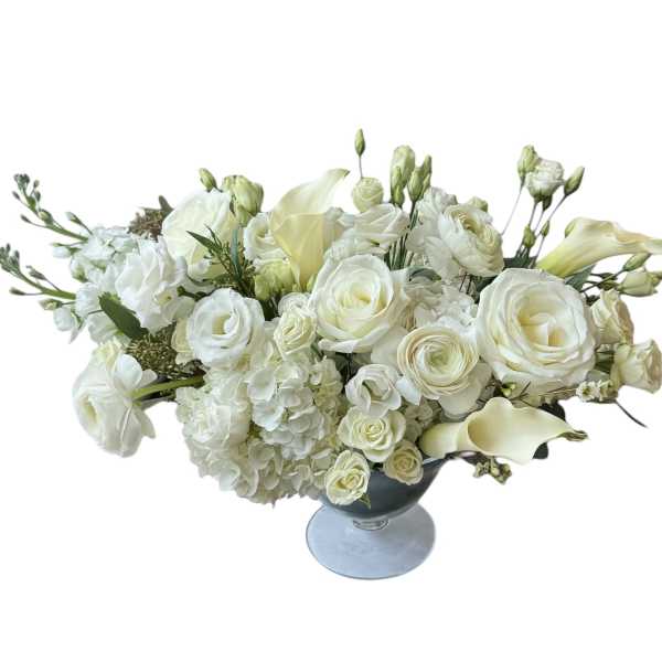 White floral arrangement in a blue glass vase with roses, calla lilies, and hydrangeas