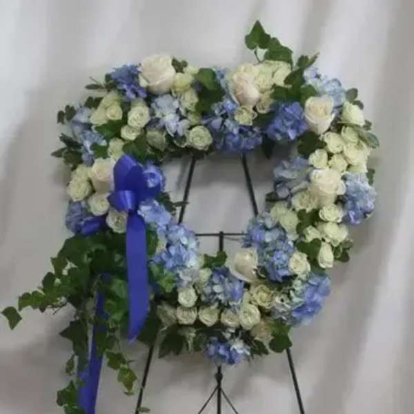 Blue and white floral wreath on a black easel with a purple ribbon