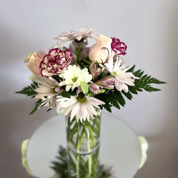 Mixed bouquet of pale daisies, carnations, and roses in a glass vase