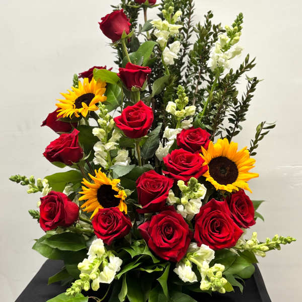 Tall arrangement of red roses, yellow sunflowers, and white snapdragons in a fan-shaped design