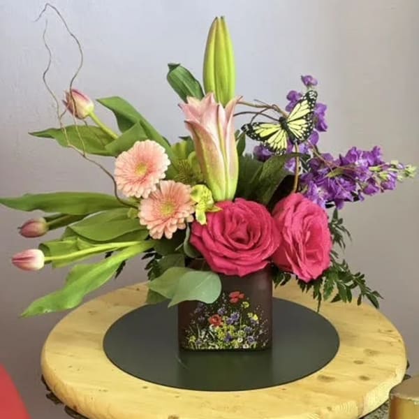 Pink roses and lilies in a square vase with a butterfly accent