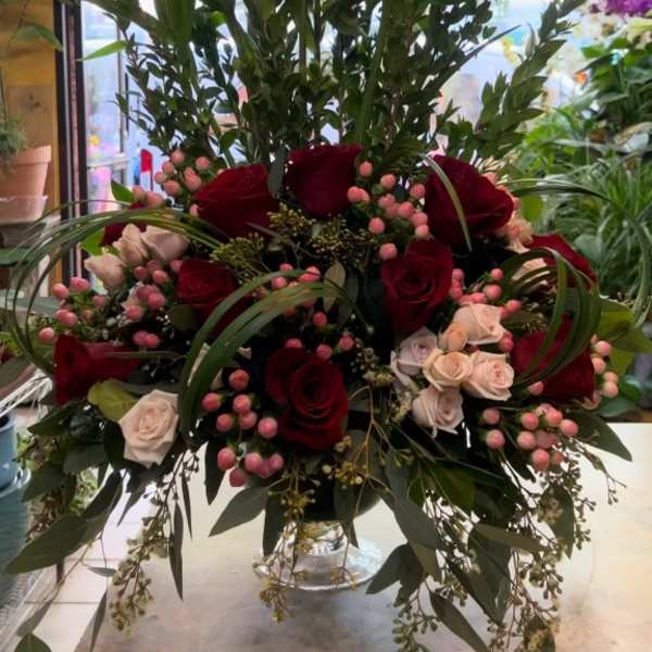 Tall arrangement of burgundy lilies and red roses in a glass vase
