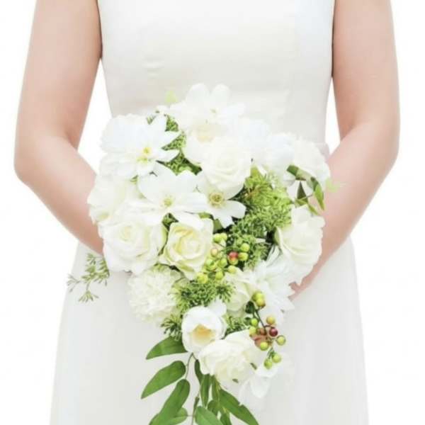 Bride in a white dress holding a cascading white rose bouquet with green accents