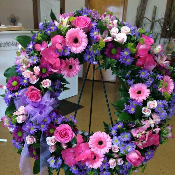 Large pink and purple floral wreath on a stand with ribbon