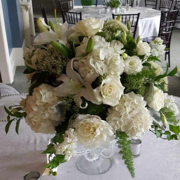 White floral centerpiece with roses, hydrangeas, and lilies in a clear vase
