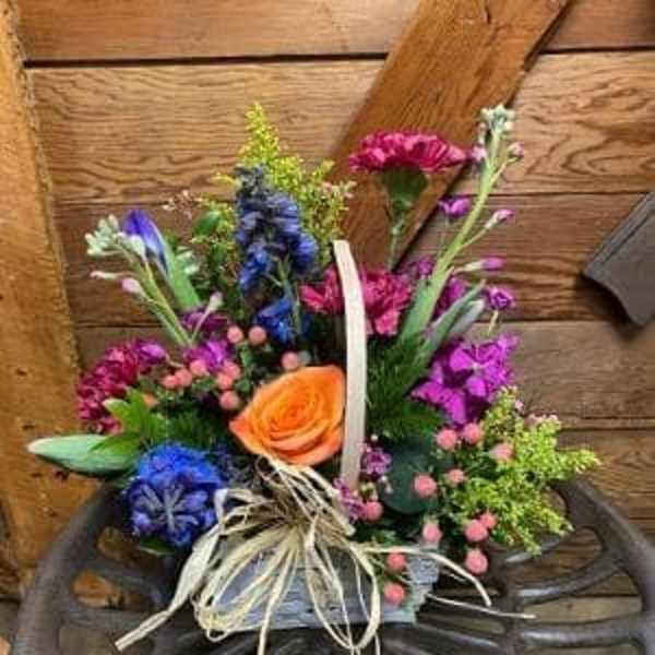 Colorful mixed bouquet with an orange rose and blue flowers in a basket