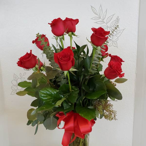 Red roses arranged in a clear glass vase with a red ribbon.