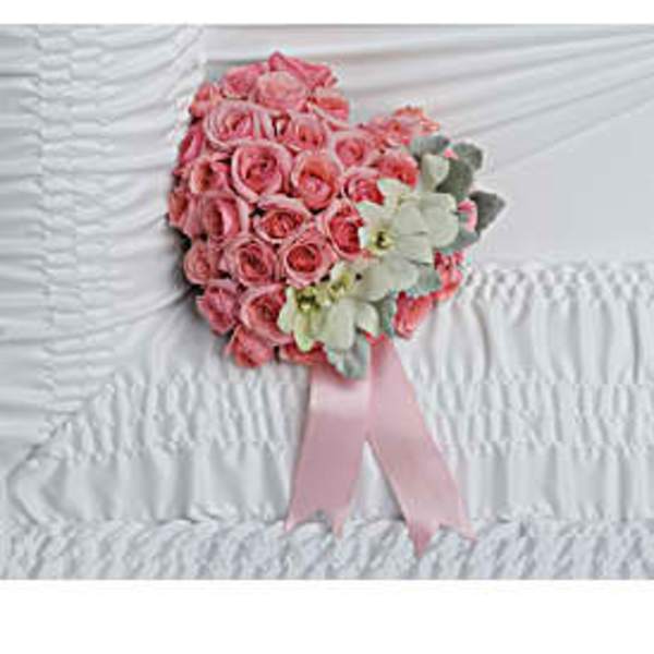 Heart-shaped pink rose arrangement with ribbon resting on white gathered fabric