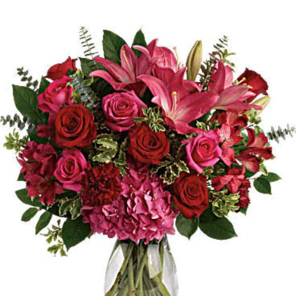 Bouquet of pink lilies, red roses, and hydrangeas in a clear glass vase