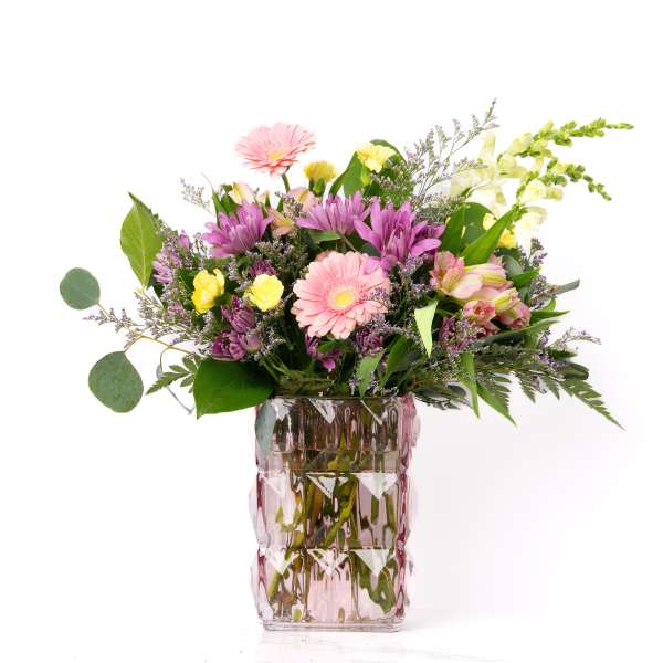 Mixed bouquet of pink gerbera daisies, purple mums, and yellow roses in a pink textured glass vase