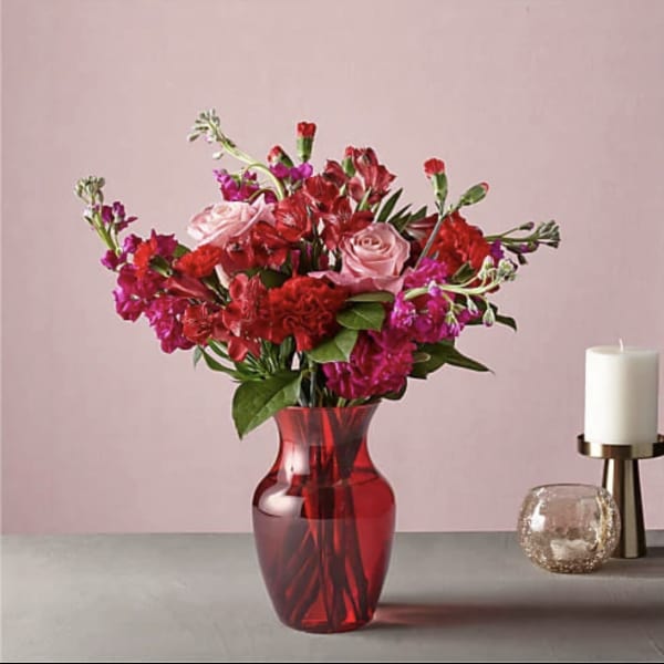 Red and pink bouquet in a red glass vase beside a candle