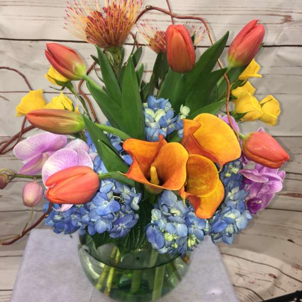 Colorful bouquet with tulips, calla lilies, orchids, and blue hydrangeas in a glass vase