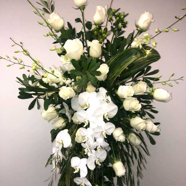 Tall white floral spray with roses and orchids on an easel