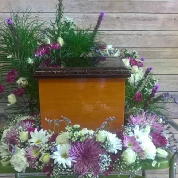 Casket surrounded by white and purple floral sprays