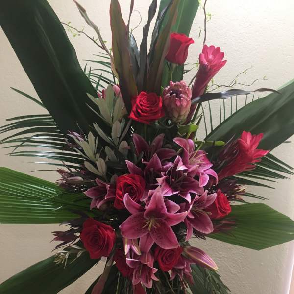 Tall arrangement of red roses and pink lilies with large tropical leaves