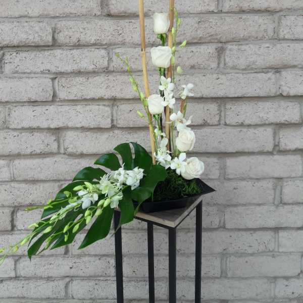 Tall white floral arrangement with roses and orchids in a black container