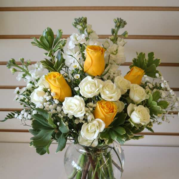 Yellow and white roses arranged in a clear glass vase
