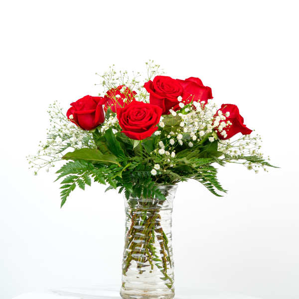 Red roses and small white flowers arranged in a clear glass vase